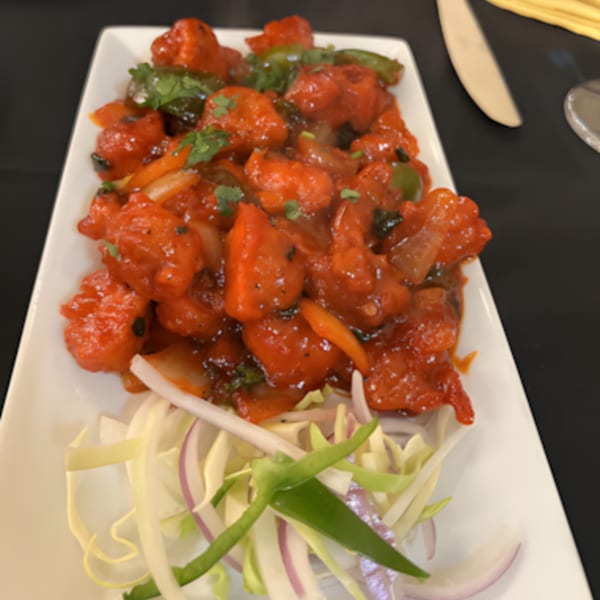 Zaika Indian Bistro Bar's bright red chili chicken, garnished with fresh cilantro and sliced onions.