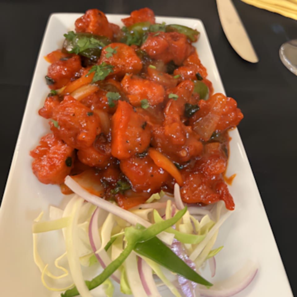Zaika Indian Bistro Bar's bright red chili chicken, garnished with fresh cilantro and sliced onions.