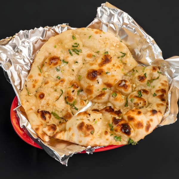 Zaika Indian Bistro Bar's garlic naan, garnished with herbs, served in foil on a red plate.